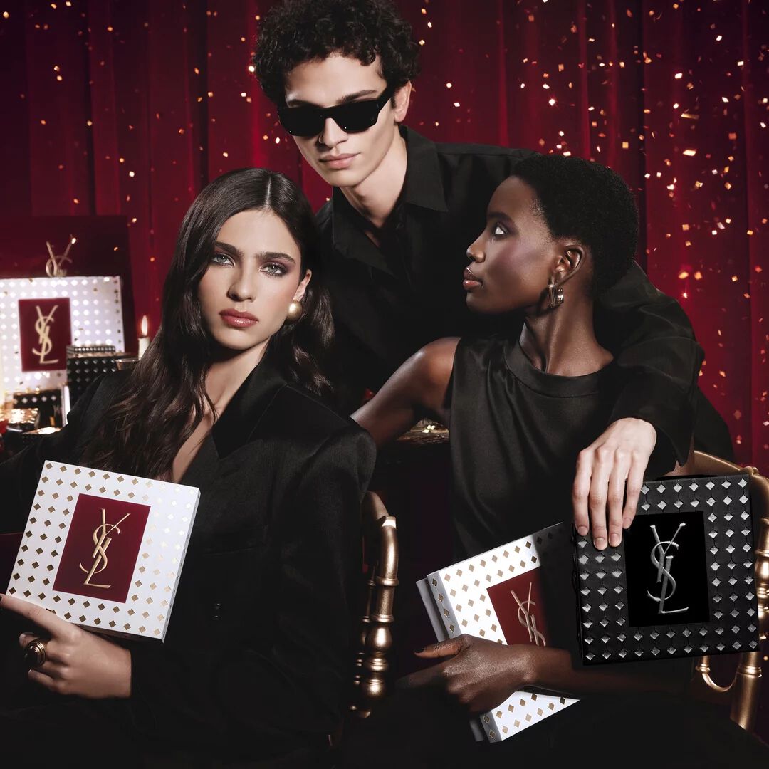 Models posing together holding luxury YSL Holiday gift boxes in a festive atmosphere.