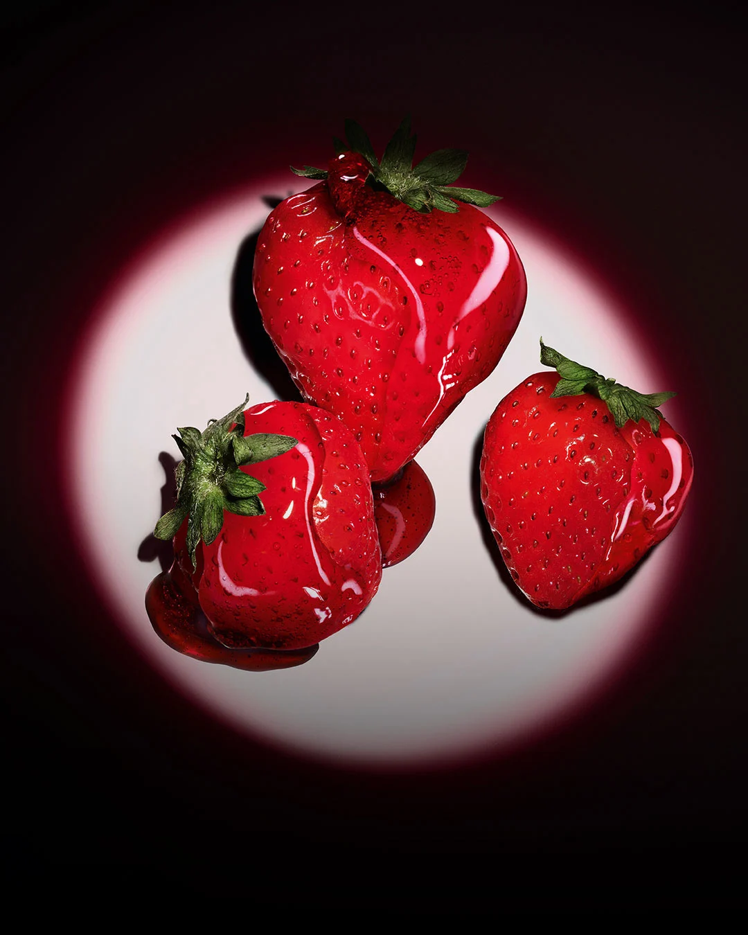 Three fresh red strawberries highlighted by a pink circular spotlight on a dark background.