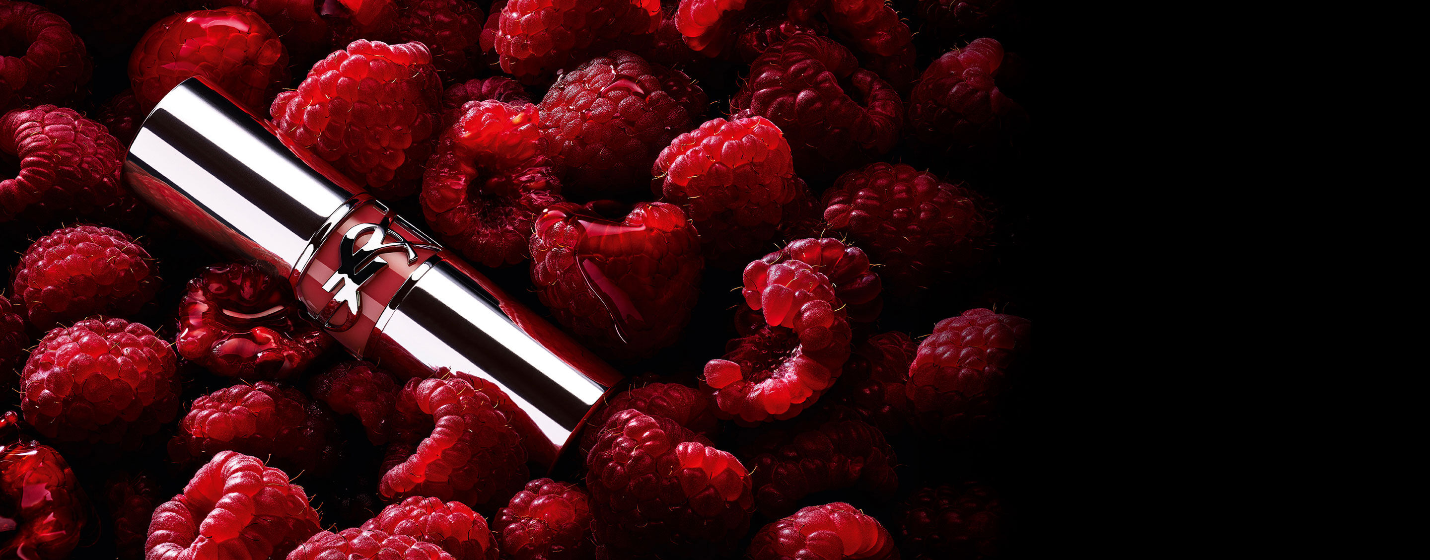 YSL LOVESHINE Berry Crush lipstick, silver tube with berry YSL logo, nestled among fresh raspberries.