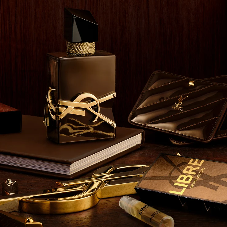 Libre Santal Couture bottle on a desk with a YSL leather pouch, a notebook, and a gold mirror.