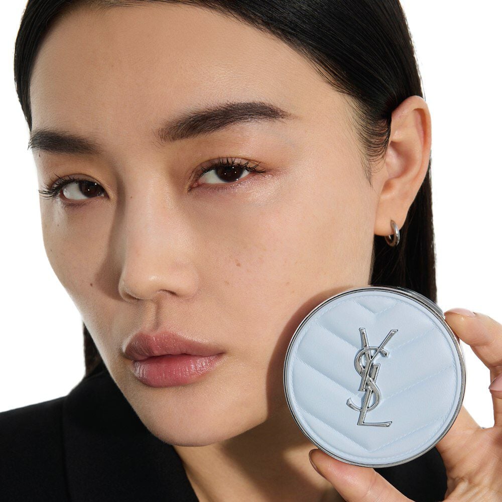 Mei J, YSL Beauty model, holding YSL All Hours Blur Cushion, showcasing its sleek light blue quilted design.