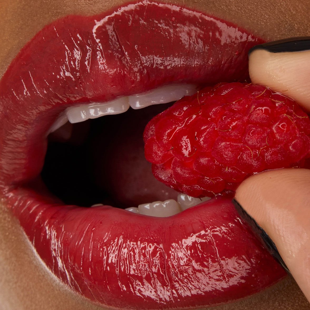 Close-up of model Zahara's lips, adorned with YSL LOVESHINE Lipstick in Berry Crush, shade 219, holding a fresh raspberry.