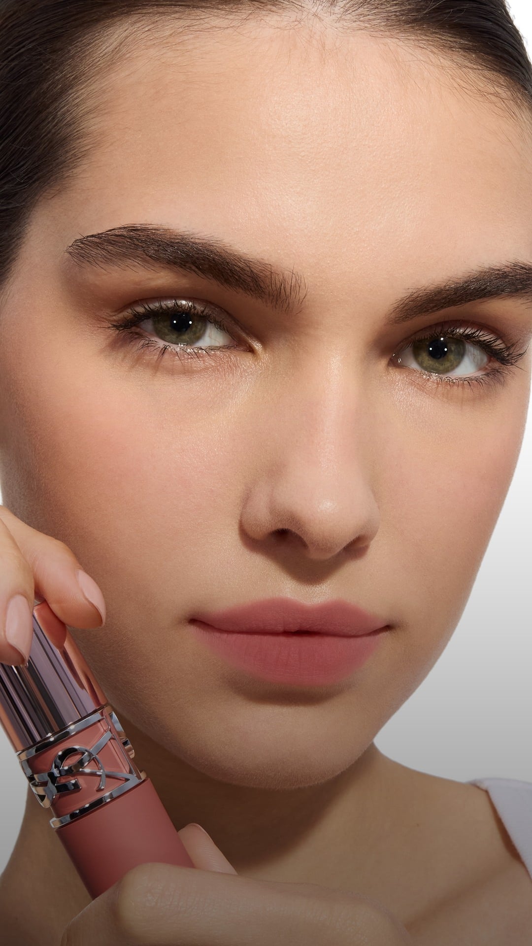 Fair skin tone model holding the YSL
LOVENUDE LIP STAIN bottle next to her
face.