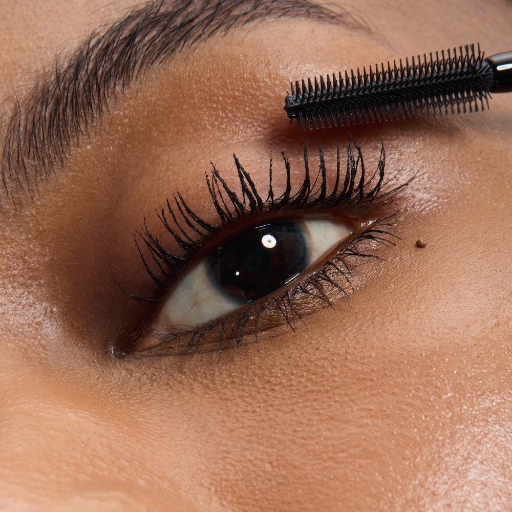 Close-up of an eye with medium skintone, showing YSL Lash Latex Mascara in shade 1 with a brush focus, applied to lashes.