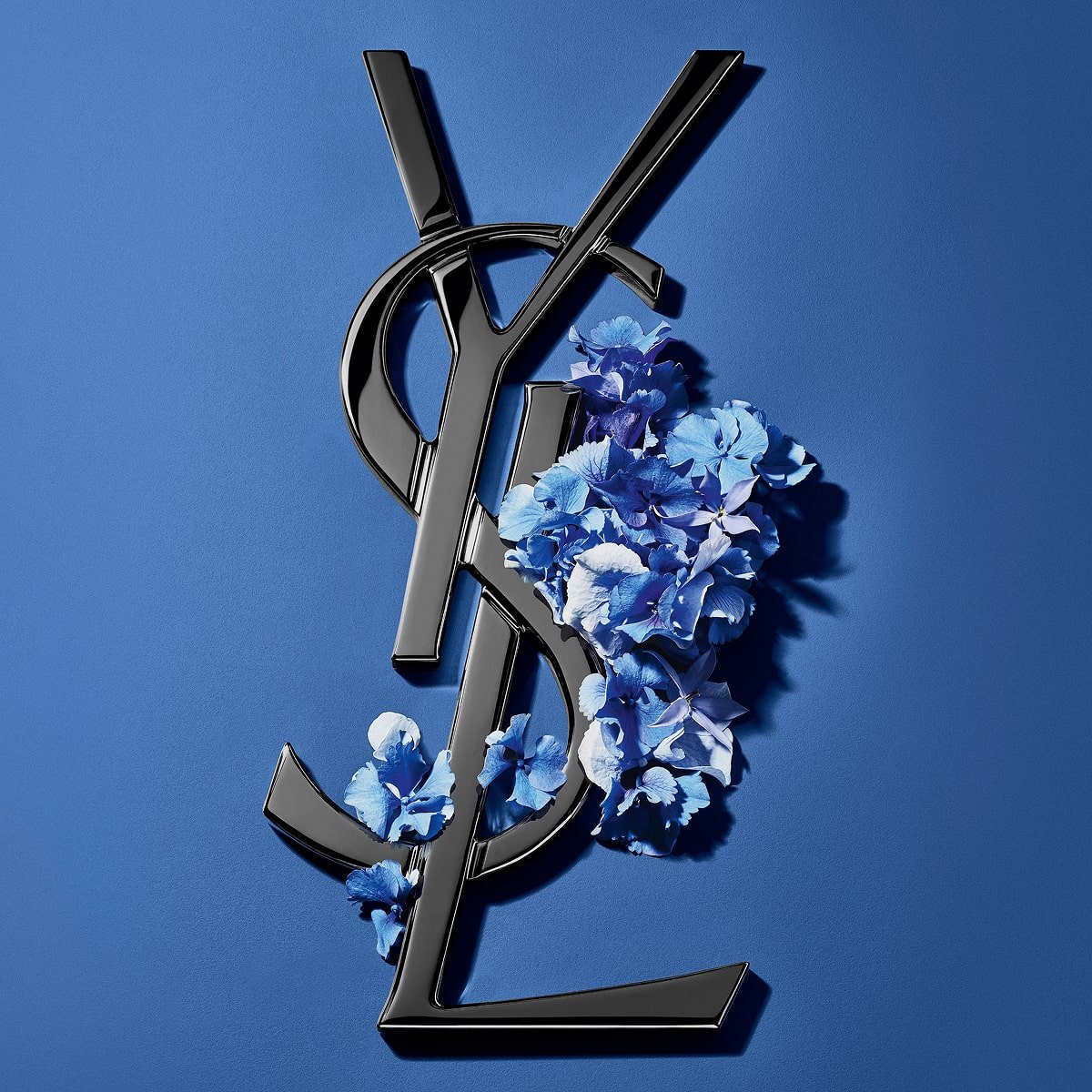 Black YSL Cassandre logo adorned with vibrant blue spring flowers, set against a serene blue background.